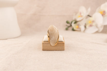 Goudkleurige ring met crèmekleurige harsknop gedragen aan een hand