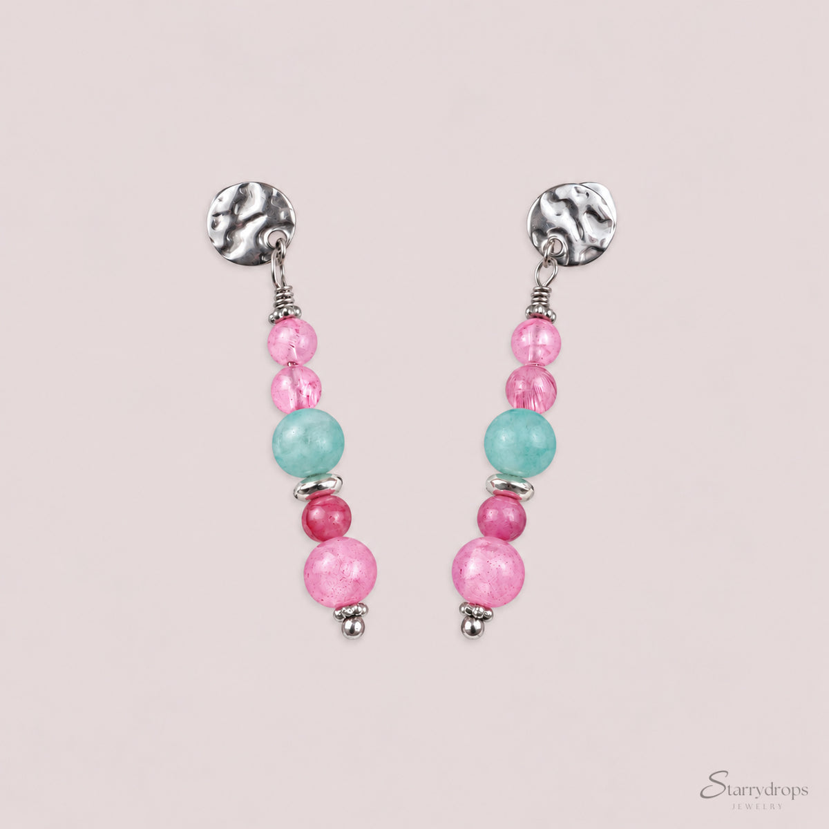 Zilverkleurige oorbellen met gehamerd stekertje en kralen in roze, blauw en fuchsia, op een beige achtergrond