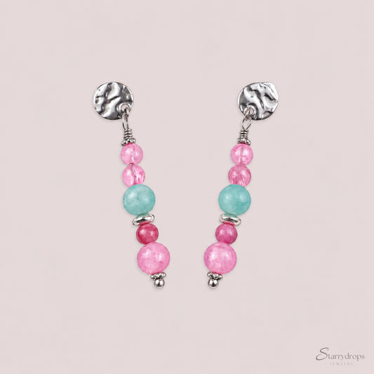 Zilverkleurige oorbellen met gehamerd stekertje en kralen in roze, blauw en fuchsia, op een beige achtergrond