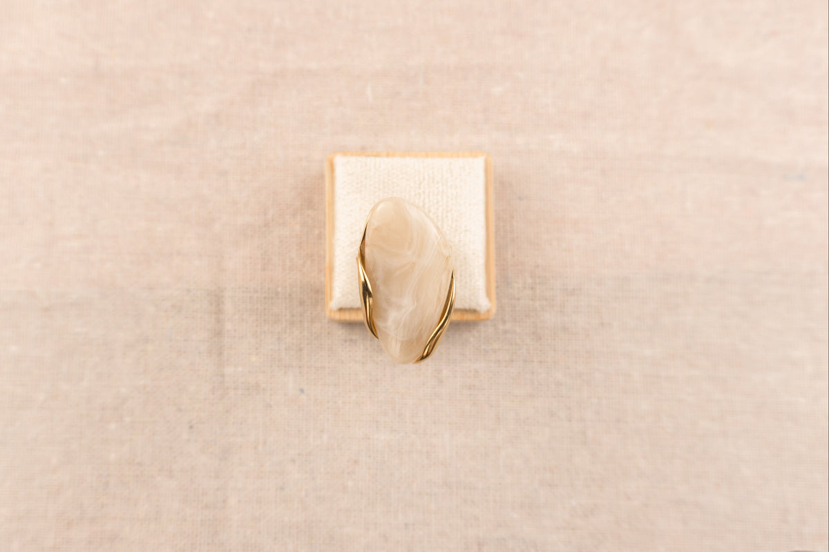 Goudkleurige ring met ronde crèmekleurige harsknop, op witte achtergrond