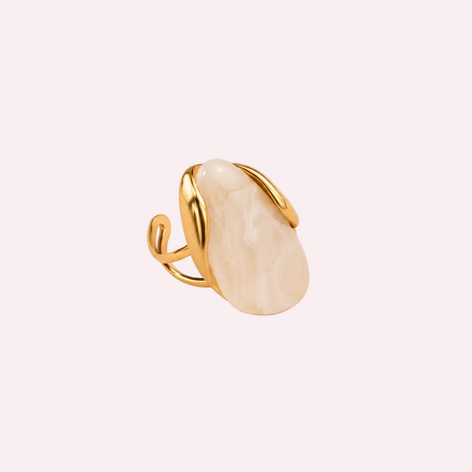 Goudkleurige ring met grote bolle crèmekleurige harsknop, organisch ontwerp, liggend op een lichte ondergrond