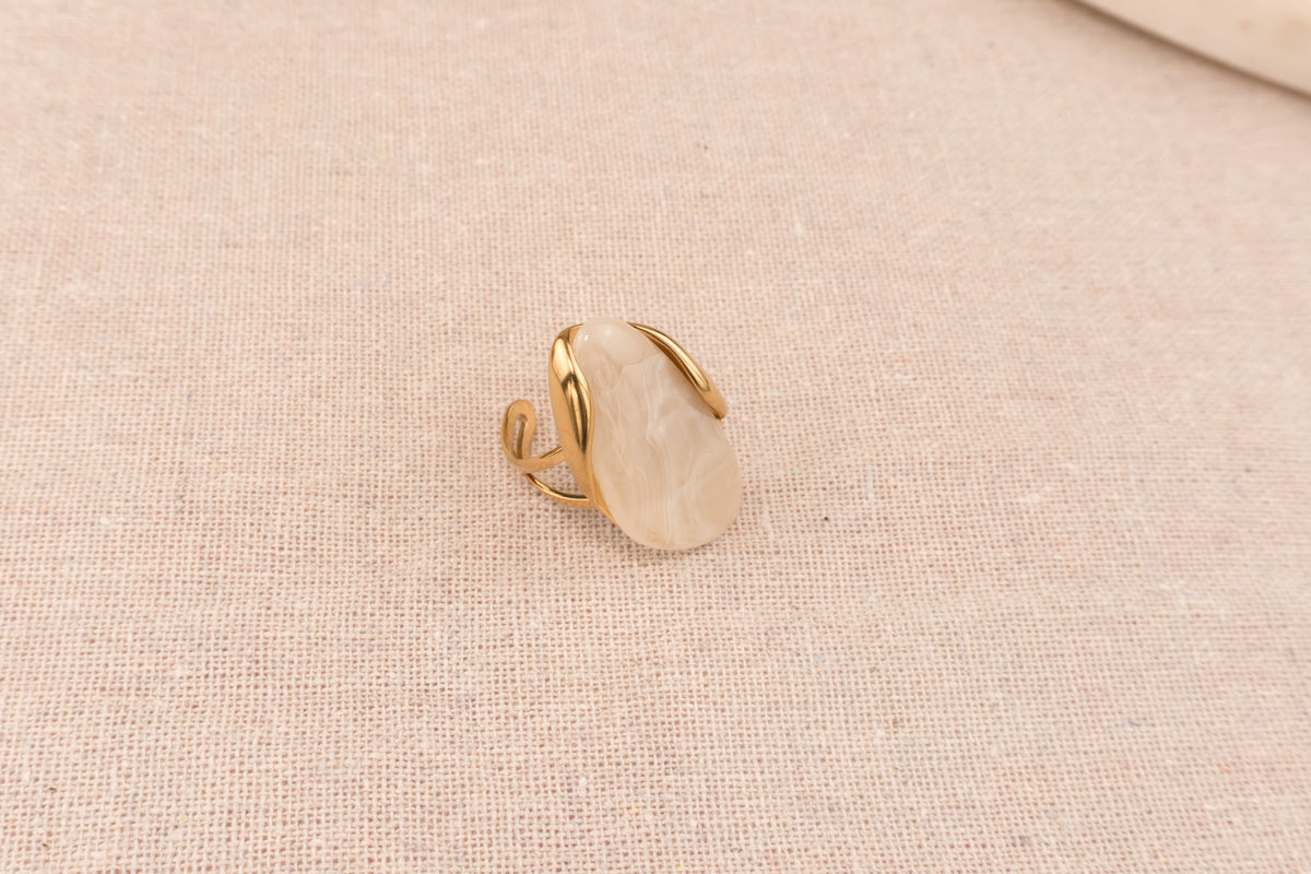 Goudkleurige ring met ronde crèmekleurige harsknop, op witte achtergrond