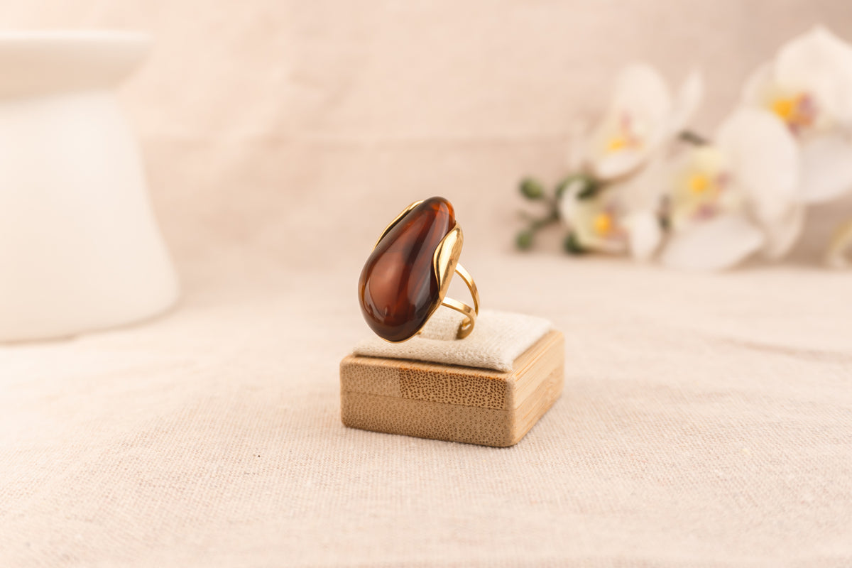 Goudkleurige ring met ovale bruine harsknop, op witte achtergrond