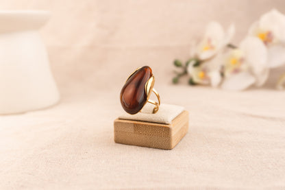 Goudkleurige ring met ovale bruine harsknop, op witte achtergrond