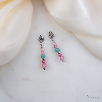 Oorbellen met roze en blauwe kralen van stainless steel, liggend op wit marmer met een crème satijnen doek