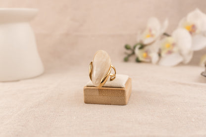 Goudkleurige ring met ronde crèmekleurige harsknop, op witte achtergrond
