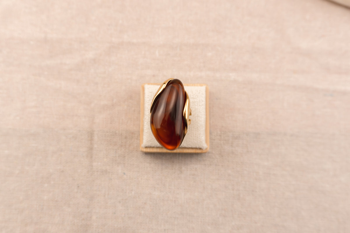 Goudkleurige ring met ovale bruine harsknop, op witte achtergrond